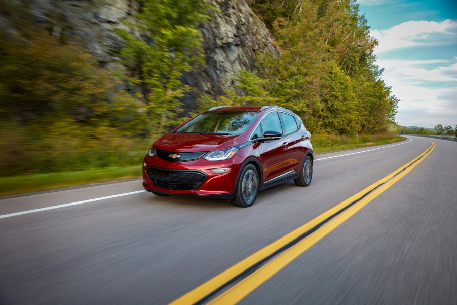 Red 2019 Chevrlet Bolt EV hatchback driving down the road next to a forest