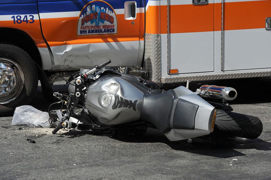 A crashed motorcycle lays in front of an ambulance