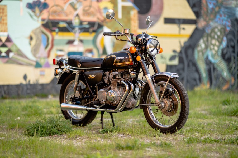 Black-with-yellow-pinstriping 1973 Honda CB350 Four motorcyle parked on lawn in front of artwork