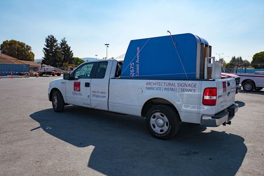 A pickup truck with a sign in the bed turning in a parking lot