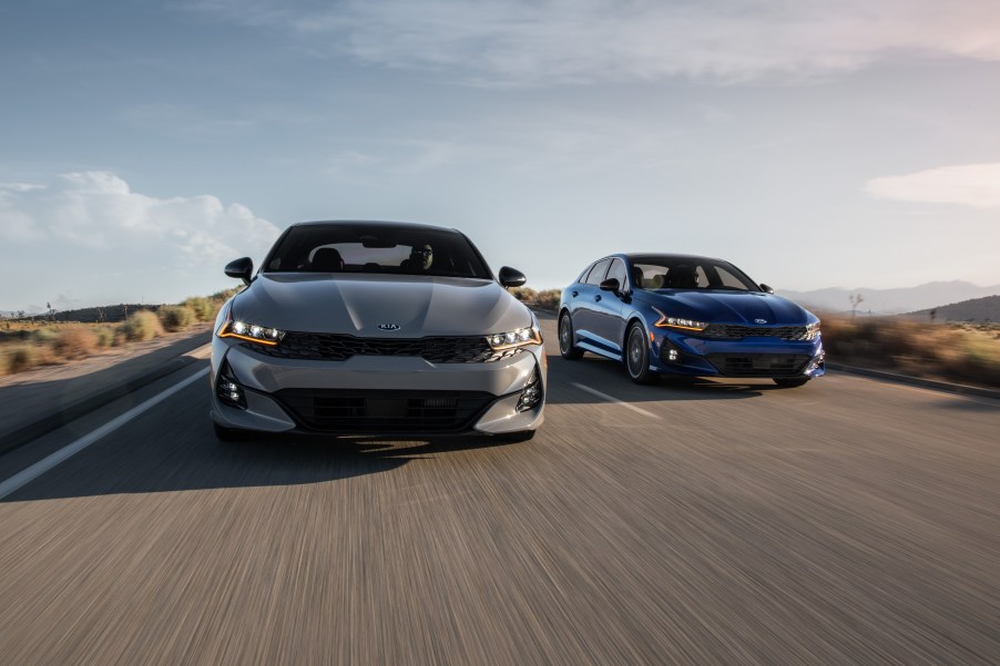 A gray 2021 Kia K5 sedan, the successor to the Kia Optima, is slightly ahead of another in this head-on picture of both cars on the road.