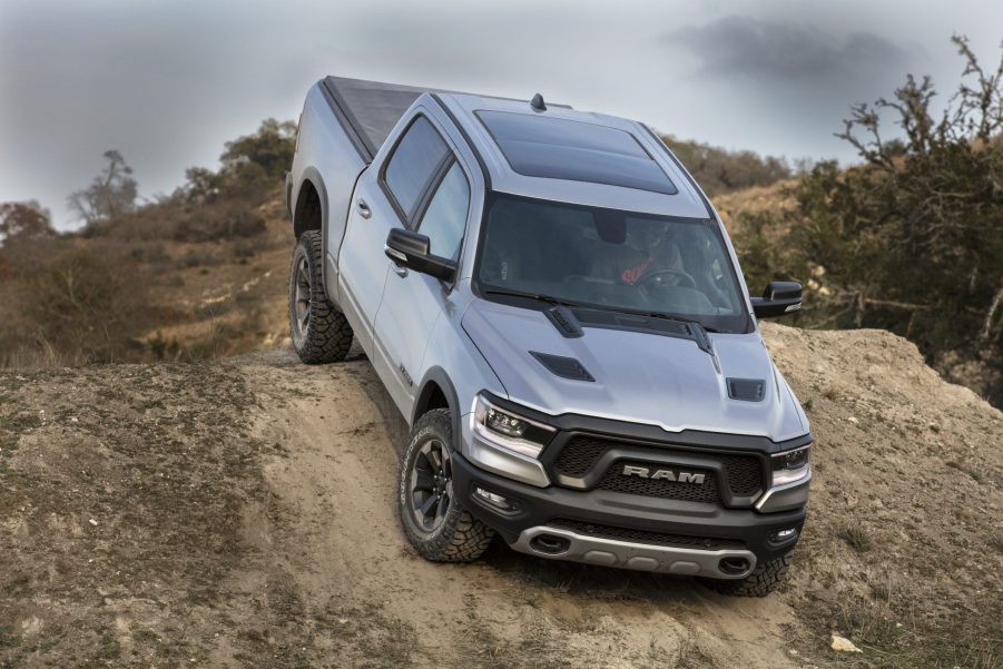 A silver Ram 1500 on a dirt road climbs over the peak of a hill.