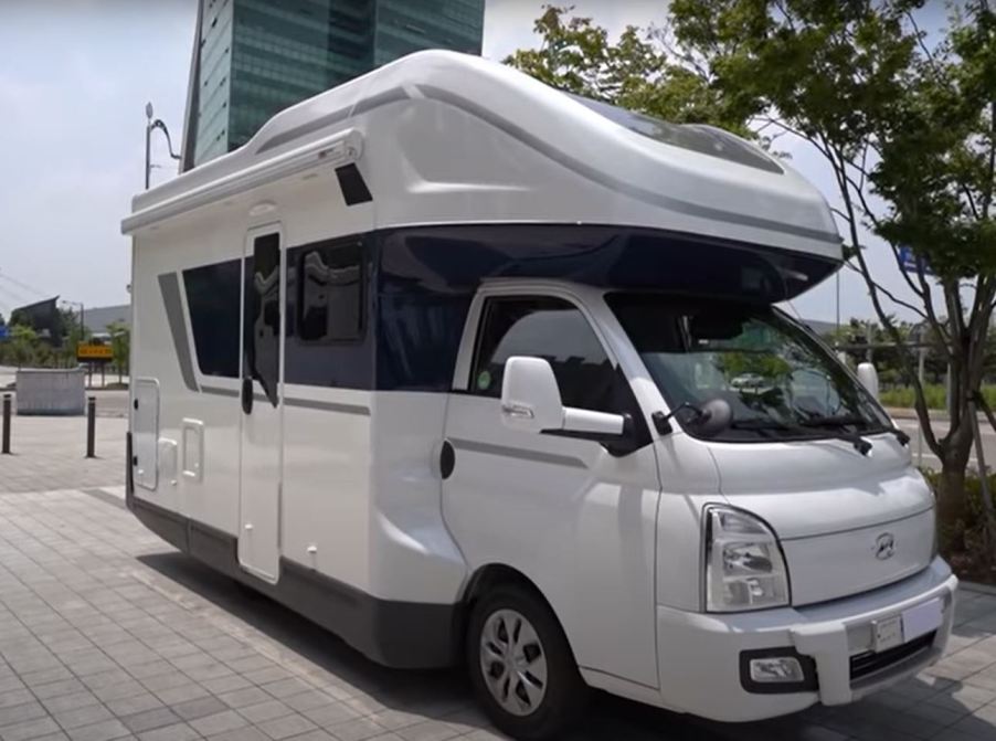 A white RV on a cab-over chassis is parked downtown.