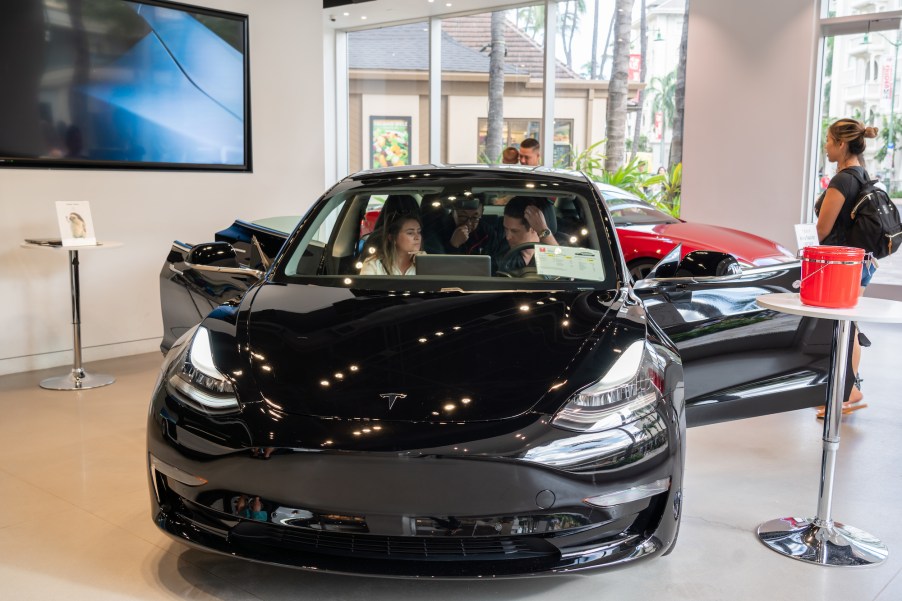 Customers admire a Tesla Model 3 electric vehicle at a Tesla store