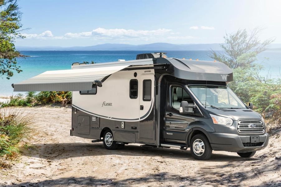 A black and white RV sits on a shore line with the awning deployed on a sunny day.