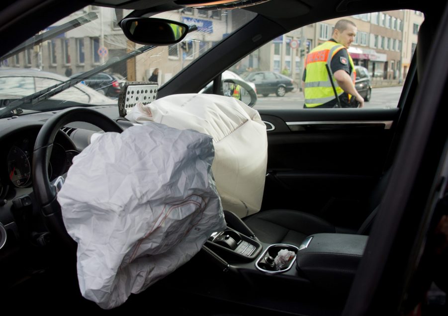 A police officer can be seen through the window of a car that has had two front airbags depoloyed.