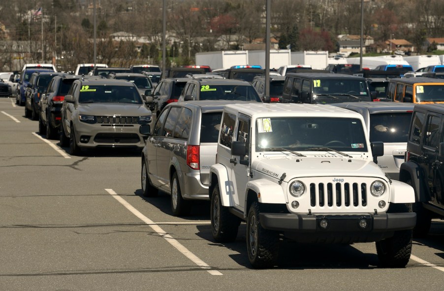 car dealership lot with a white jeep and other cars with model years and prices highlighted