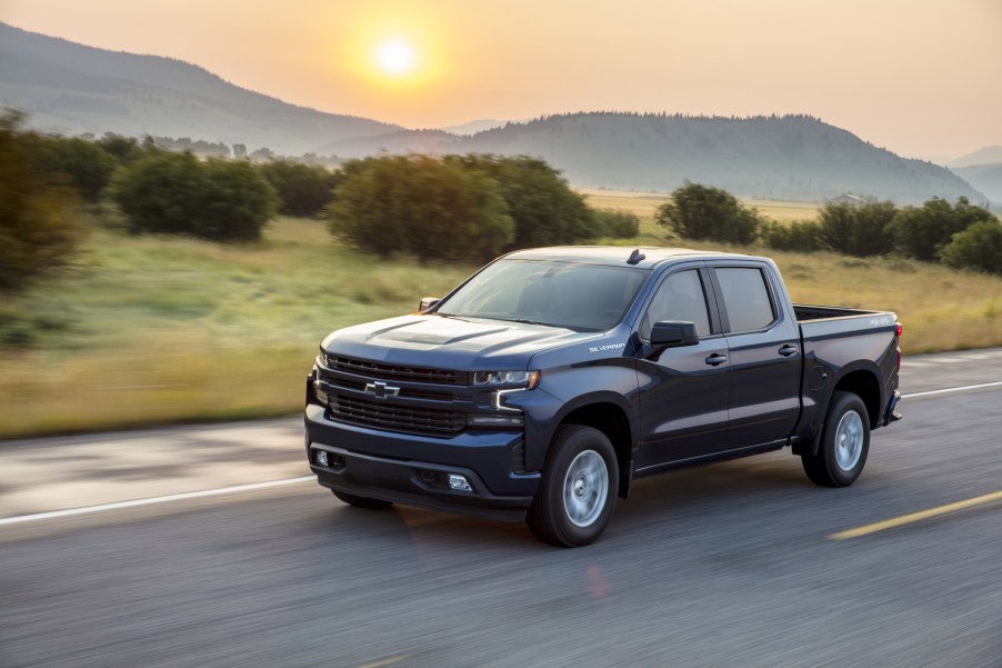 A 2020 Chevy Silverado 1500 driving on the road with trees and the sun in the background