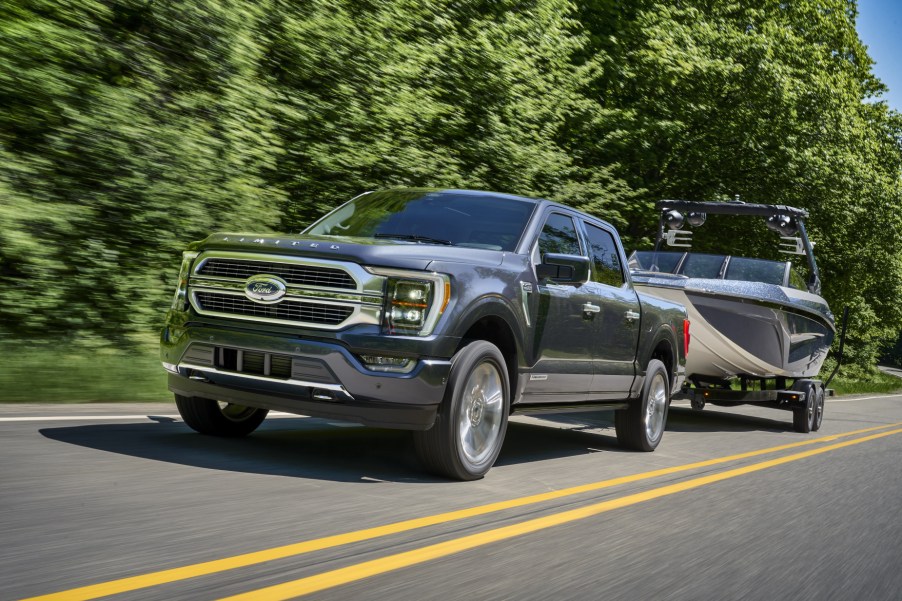 A grey 2021 Ford F-150 PowerBoost towing a boat on highway