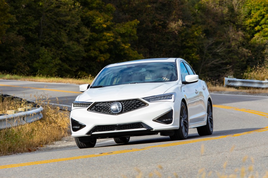 A white 2021 Acura ILX A-Spec drives on a winding country road