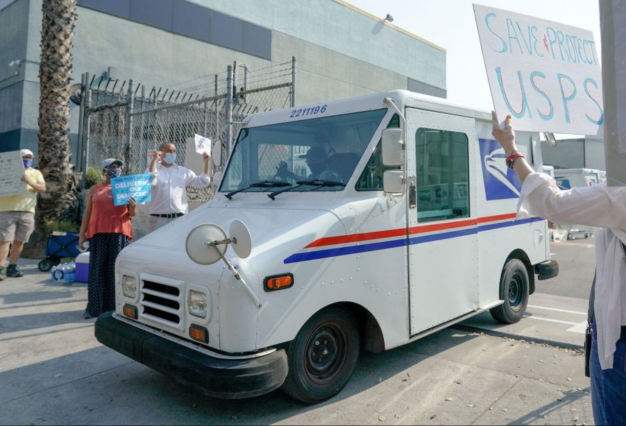 An image take just outside of a USPS dispatch center where trucks and workers are loading packages.