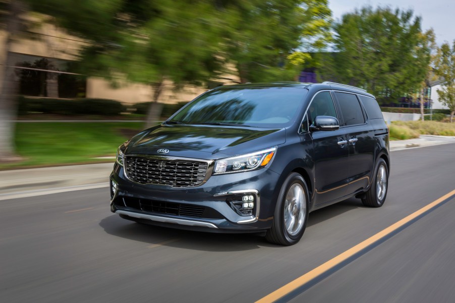 A dark-colored 2021 Kia Sedona travels on a suburban street