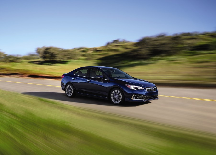 A dark-blue 2021 Subaru Impreza sedan travels on a paved road flanked by grass and bushes