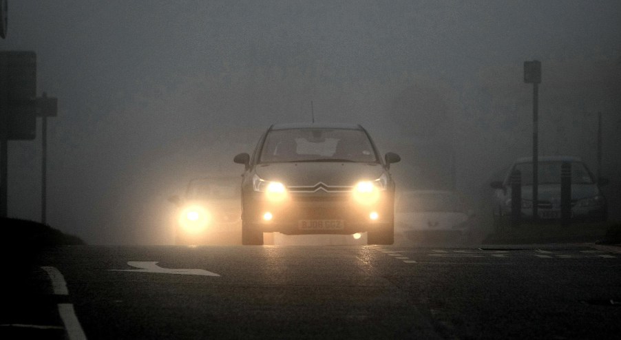 A Citroen with its fog lights on drives on a foggy British roadway