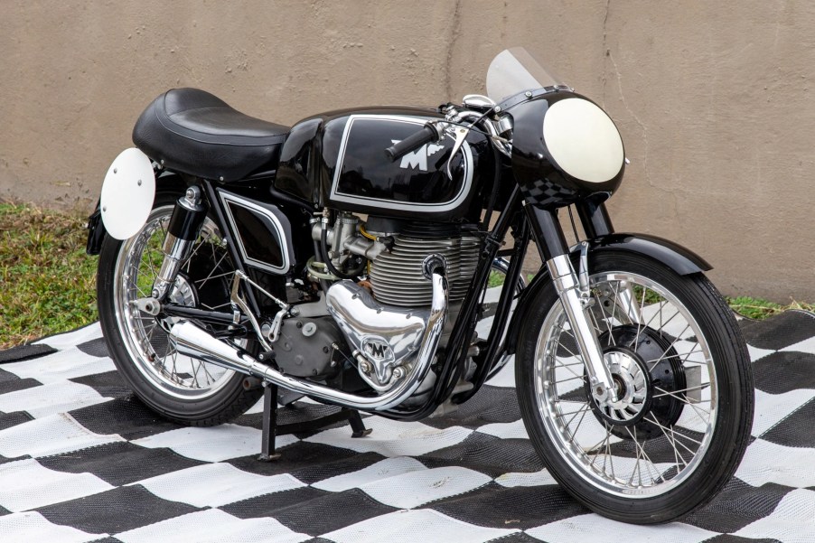 A black 1956 Matchless G45 production race motorcycle by a wall on a black-and-white checkerboard