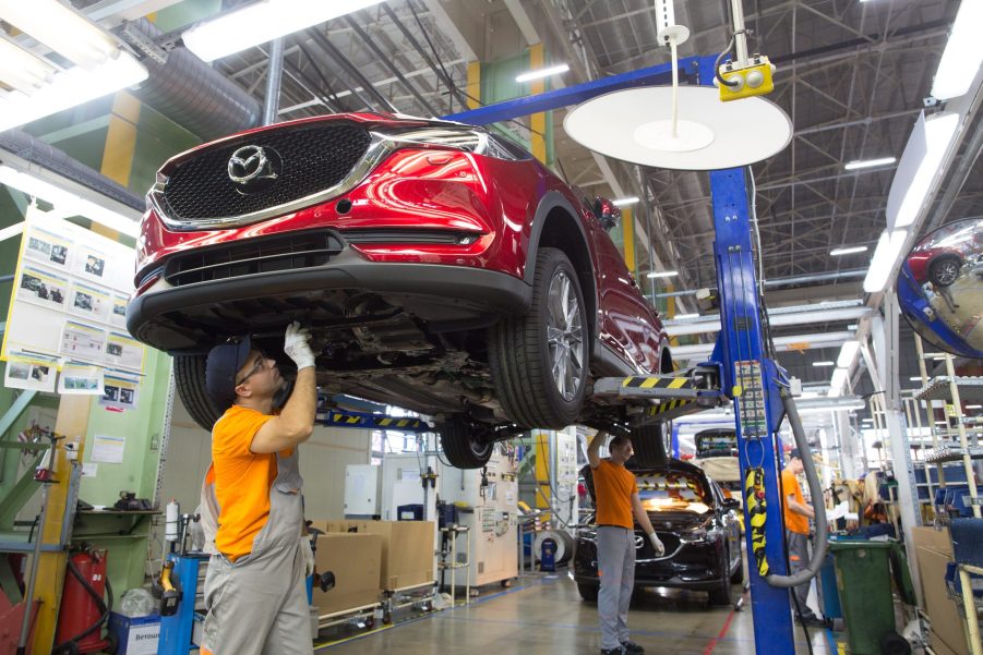 Workers affix parts to the underside of a Mazda Motor Corp. CX-5 sports utility vehicle (SUV) on the assembly line at the Mazda Sollers Manufacturing Rus LLC plant in Vladivostok, Russia, on Tuesday, Sept. 3, 2019