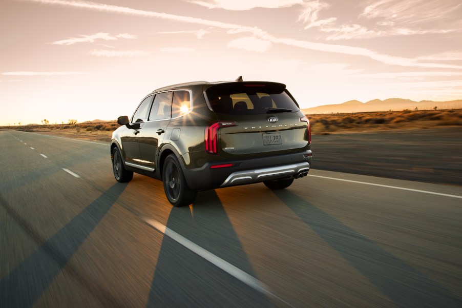 A side-rear view of a dark-colored 2020 Kia Telluride midsize SUV driving into the sunset