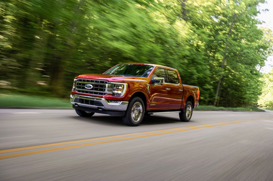 A metallic-red 2021 Ford F-150 Lariat four-door pickup truck traveling on a two-lane highway past thick trees on a sunny day