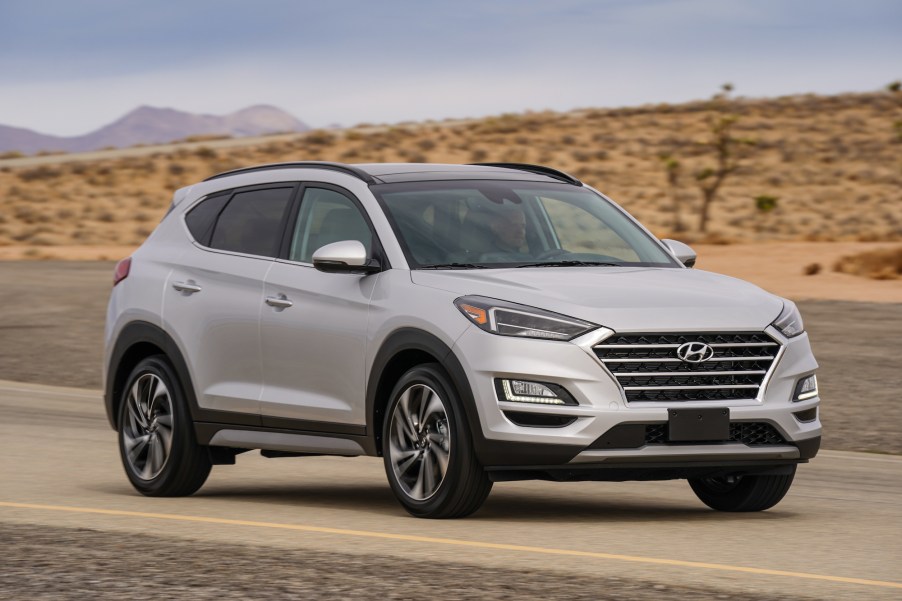 A silver 2021 Hyundai Tucson compact SUV travels on a desert road with mountains in the background