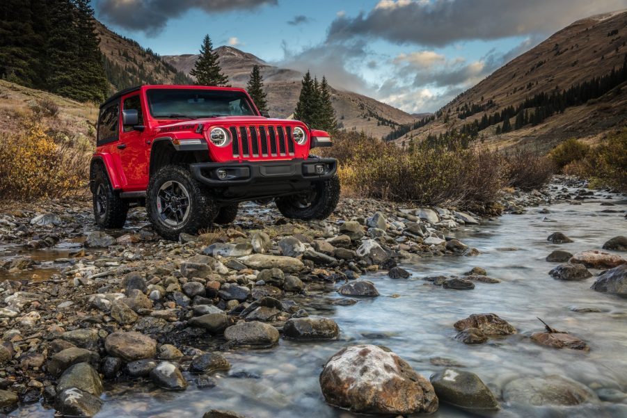 An orange 2021 Jeep Wrangler Rubicon parked on rocky terrain next to a river