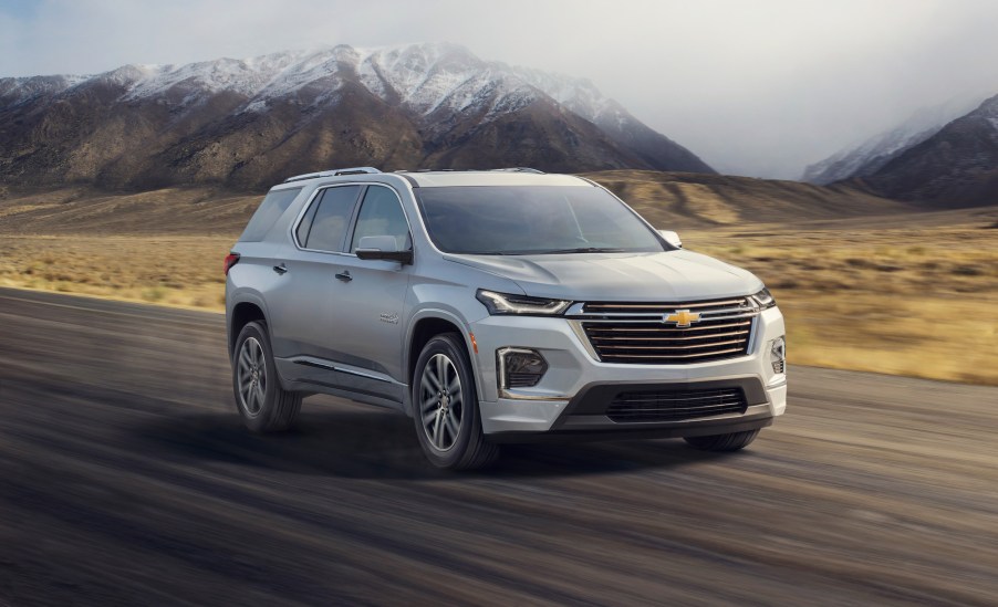 A light-colored 2022 Chevrolet Traverse High Country three-row midsize SUV traveling on a road past snow-capped mountains