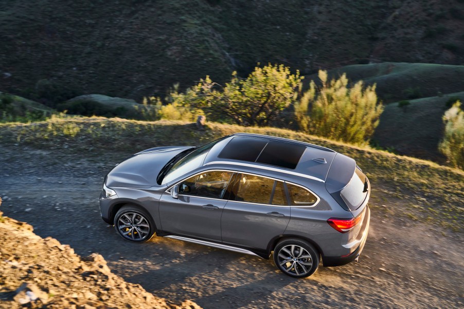 A gray BMW X1 luxury SUV travels on a dirt road on a mountain