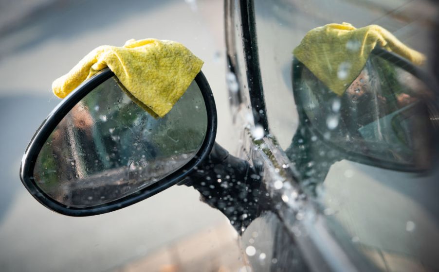 A yellow microfiber towel rests on the sideview mirror of a wet car