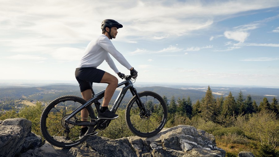 A white-clad rider on a black Porsche eBike Cross on top of a forest hill