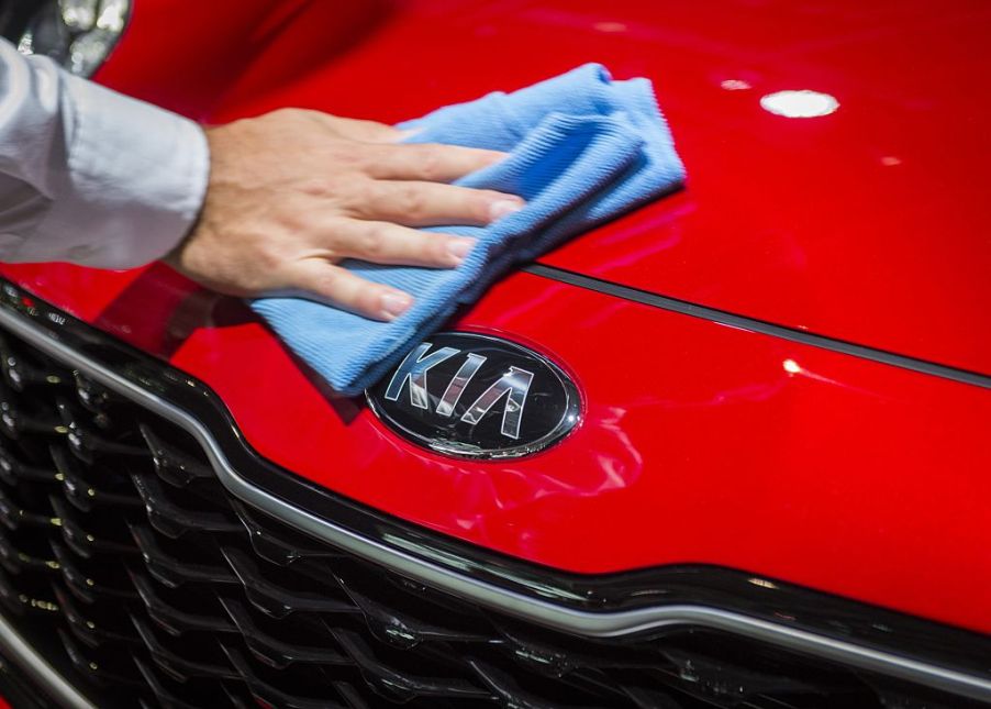 A man wipes down the front end of a red kia sportage