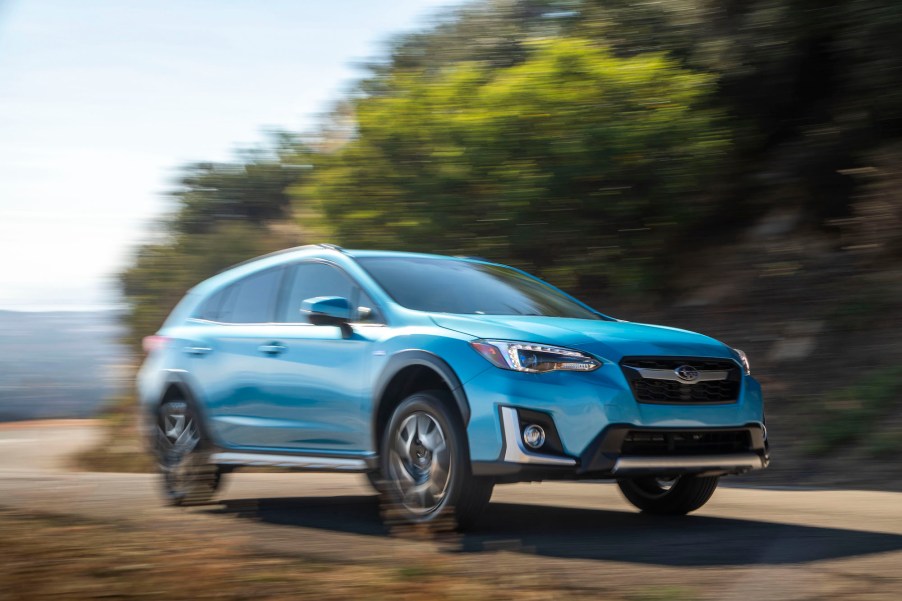 A sky-blue 2020 Subaru Crosstrek Hybrid crossover SUV traveling on a curving road near a large body of water on a sunny day