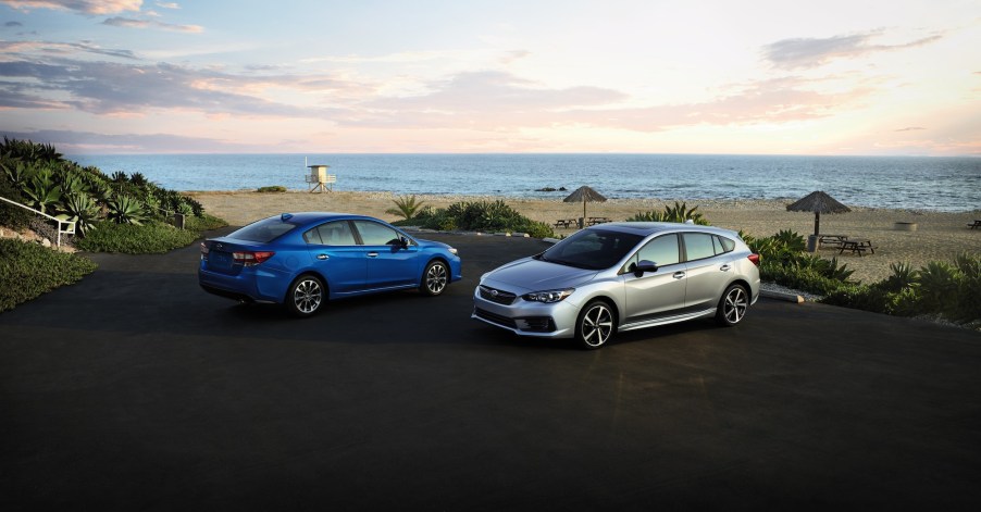 A blue 2020 Subaru Impreza sedan and a silver 2020 Subaru Impreza hatchback in a parking lot overlooking a beach