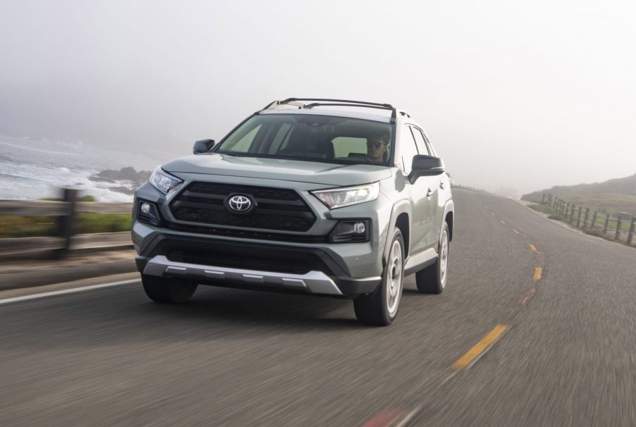 A gray and white 2021 Toyota RAV4 Adventure compact SUV traveling on a two-lane road overlooking a large body of water on a foggy day