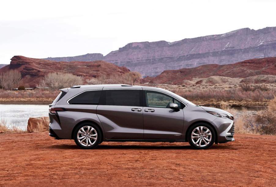 A pewter-colored 2021 Toyota Sienna Platinum hybrid minivan parked in red dirt and a small lake in front of mountains