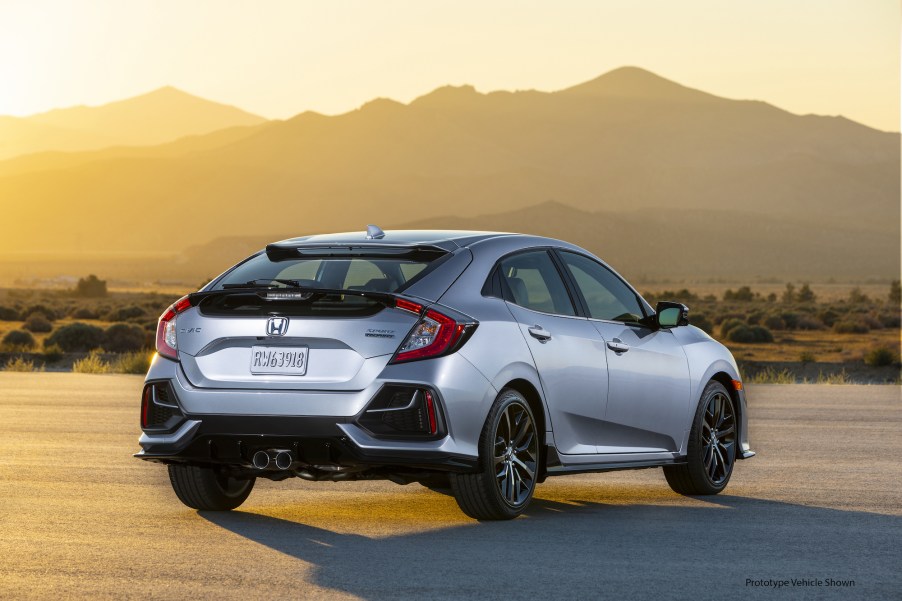 A silver 2021 Honda Civic Hatchback Sport Touring parked in front of mountains and the sun