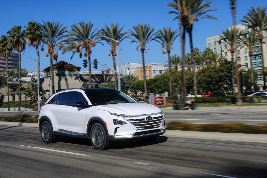 A white 2021 Hyundai Nexo compact crossover SUV traveling on a city street lined with palm trees