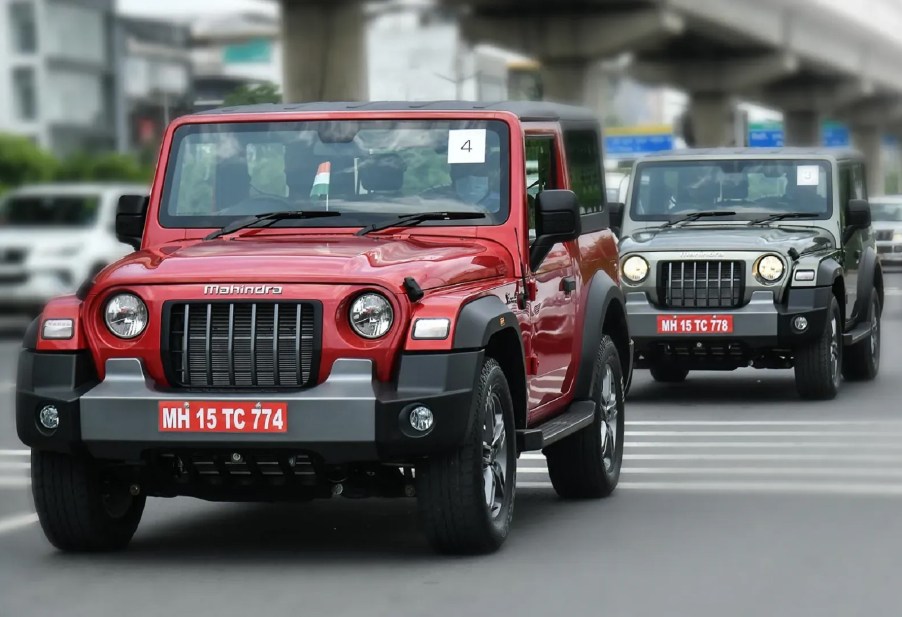 A red 2021 Mahindra Thar driving in front of a gray 2021 Mahindra Thar on an Indian city road