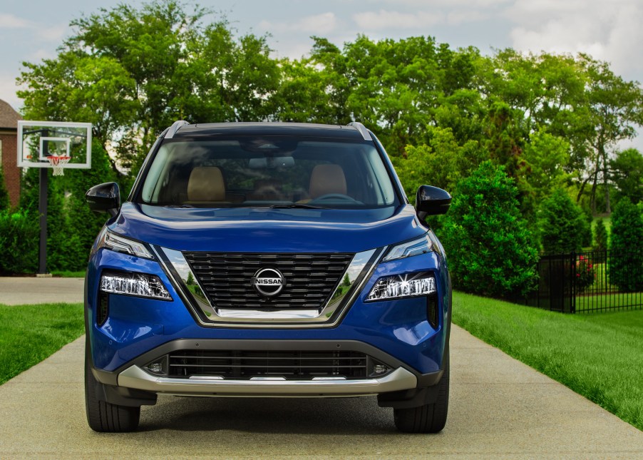 A blue 2021 Nissan Rogue parked in a suburban driveway with a basketball hoop