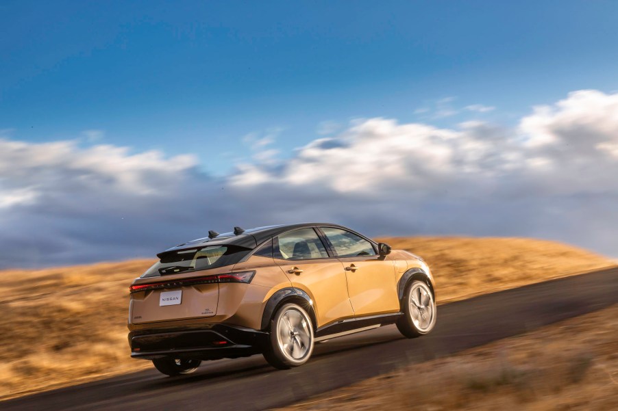 A gold 2022 Nissa Ariya electric compact SUV traveling uphill on a partly sunny day