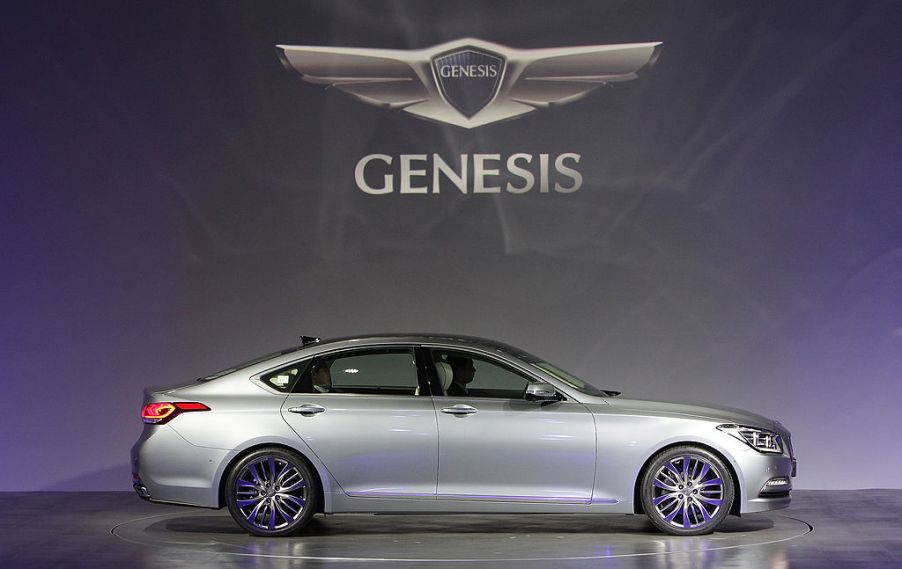 A silver Genesis sedan on stage with the Genesis logo in the background