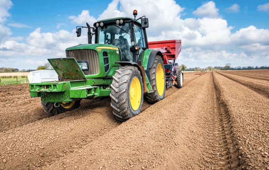 a green John Deere tractor with yellow wheels doing framework in a bare field