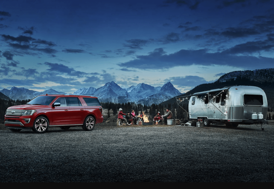 A red 2021 Ford Expedition parked at a campsite with an Airstream trailer