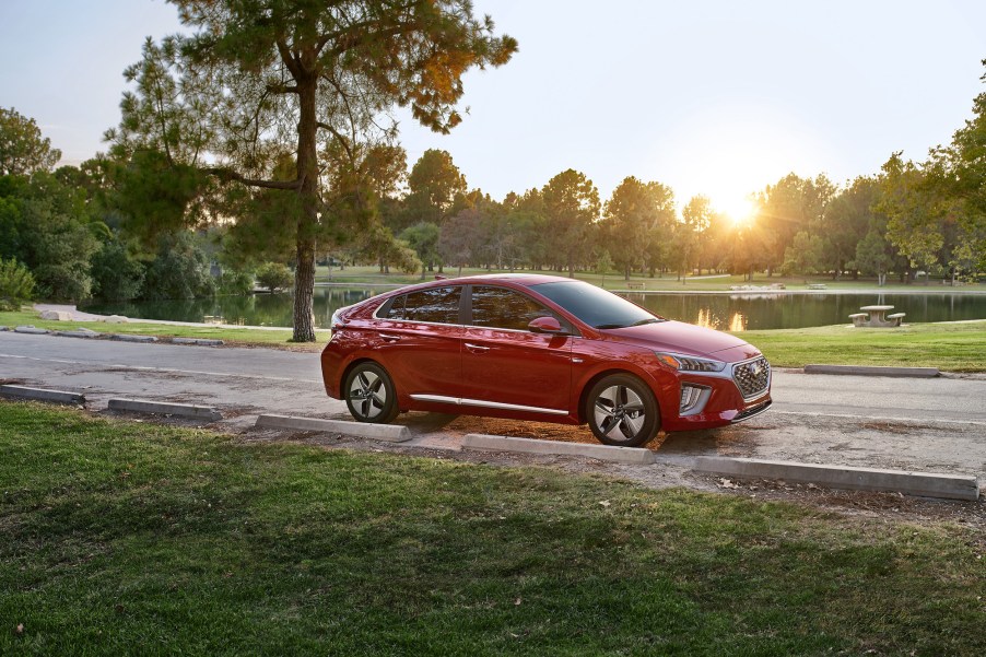 A red 2021 Ioniq Hybrid sedan parked on a road overlooking a lake and trees as the sun hangs low in the sky