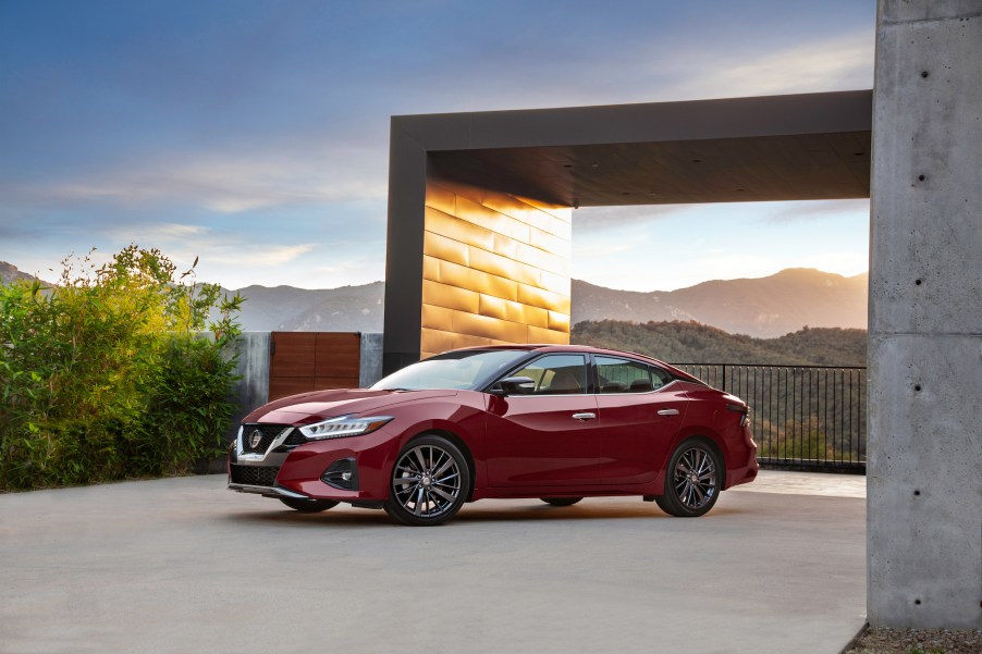 A red 2021 Nissan Maxima sedan parked outside a modern concrete home overlooking mountains