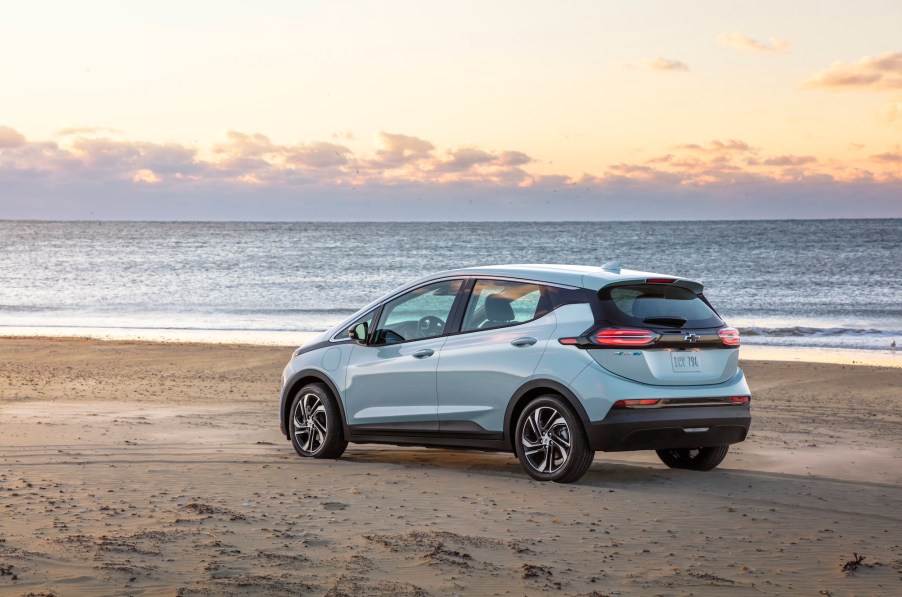 A silver 2022 Chevy Bolt EV hatchback parked on a beach overlooking an ocean as the sun sits below the horizon