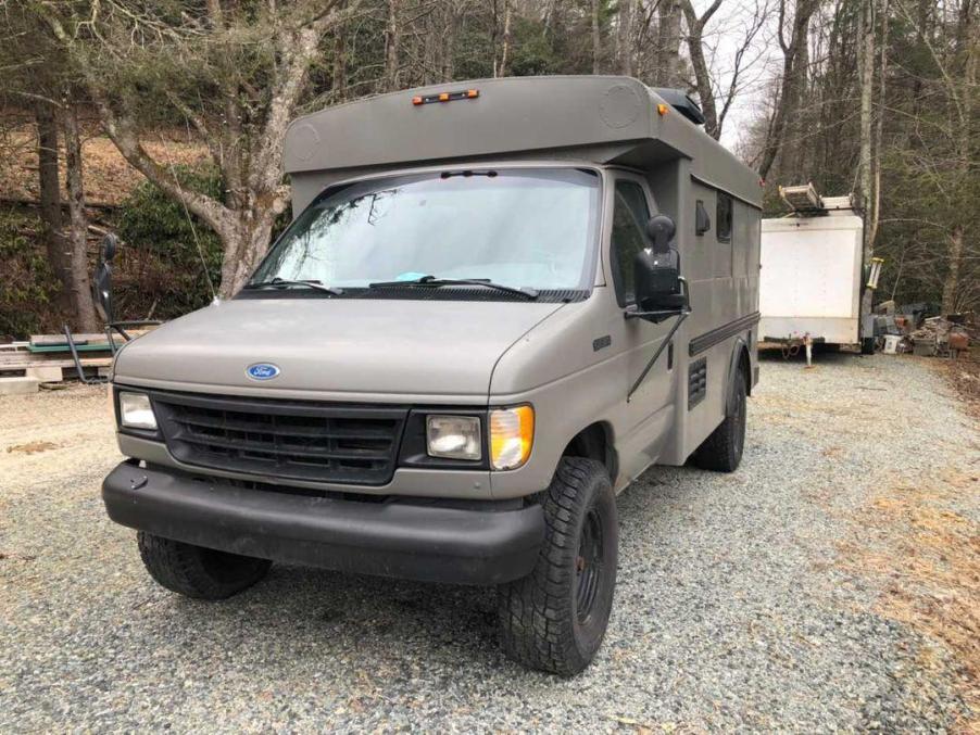 Ford E350 minibus camper conversion in a grayish green, parked on a gravel drive.