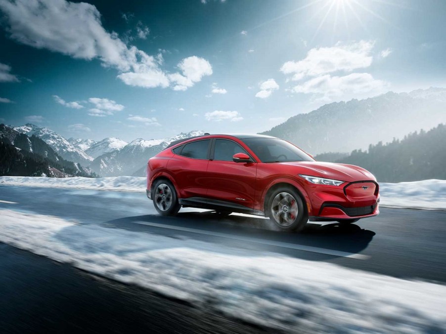 A red 2021 Ford Mustang Mach-E drives down a snow-lined road.