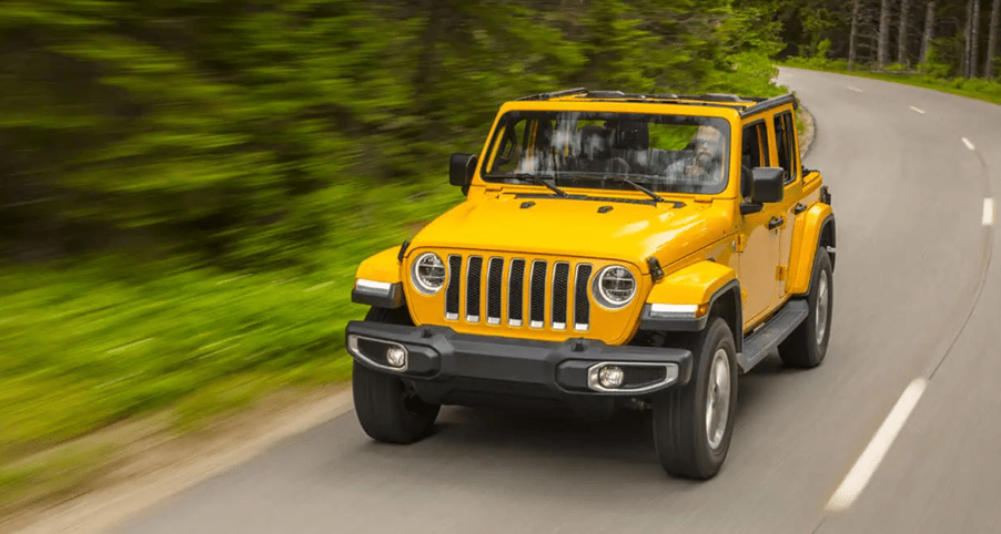 A yellow 2021 Jeep Wrangler driving on a road in the woods