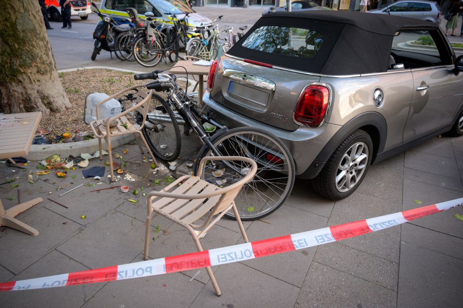 A rental car involved in an accident is parked among bicycles, tables, chairs and destroyed crockery