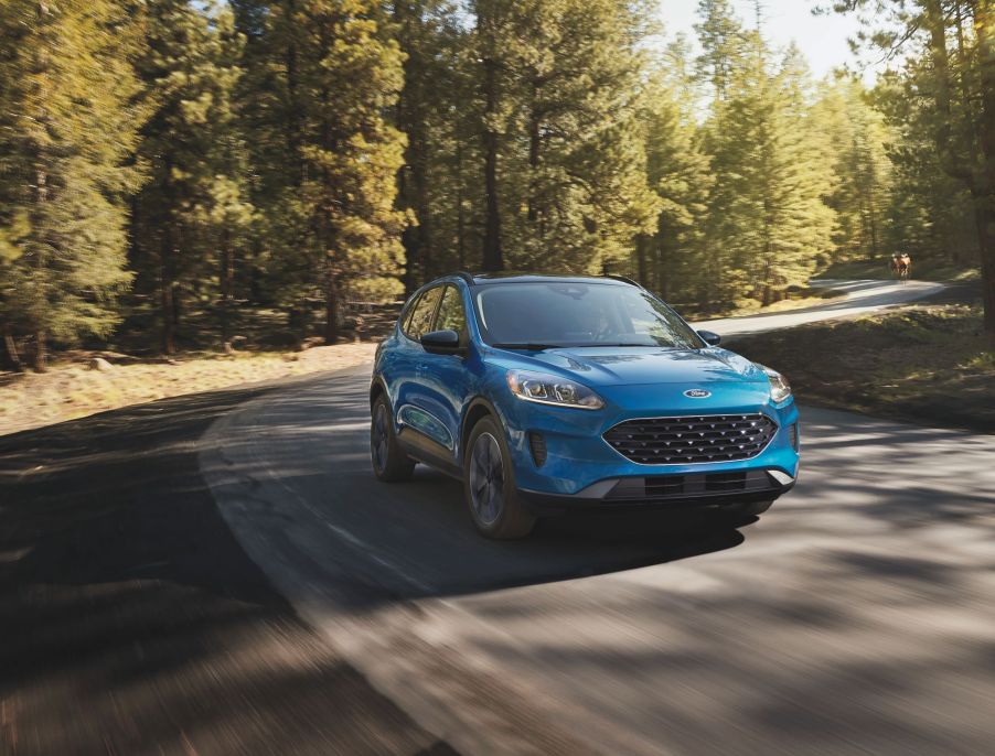 A teal 2021 Ford Escape Driving on a highway in a very wooded area.