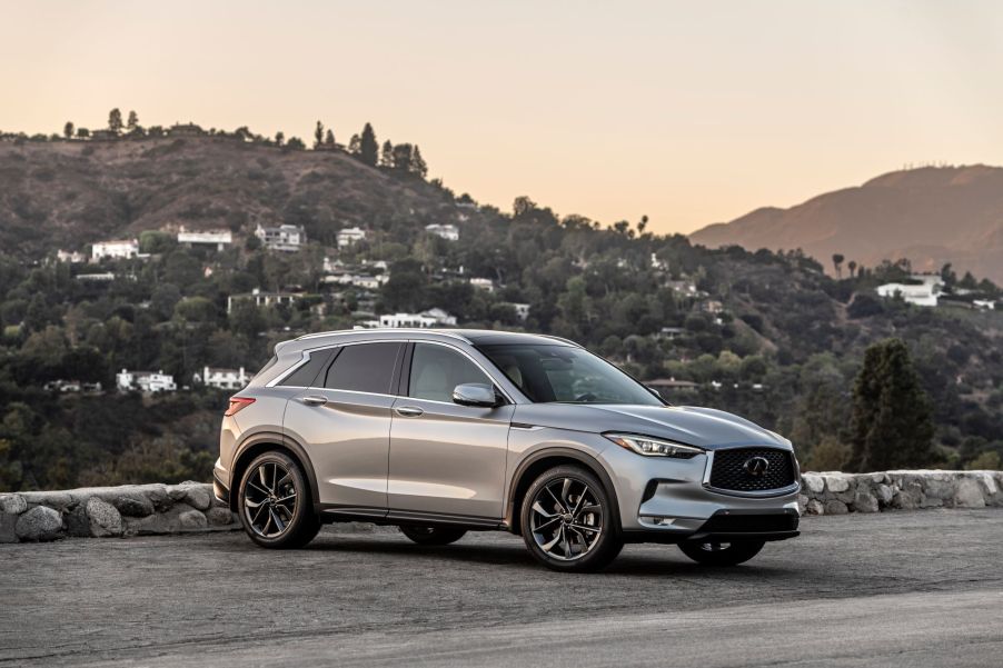 A 2021 Nissan Infiniti QX50 parked on a highway in front of a mountain with scattered houses on it.